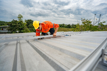 Technician in safety uniform and helmet kneeling on a rooftop, using a drill for precise...