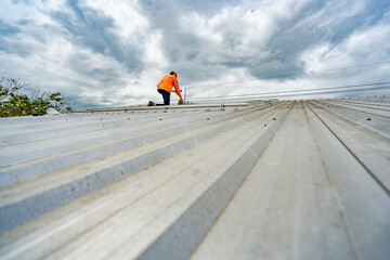 Technician in safety uniform and helmet kneeling on a rooftop, using a drill for precise...