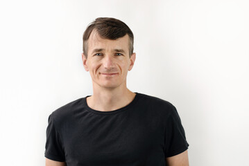 Fototapeta premium Smiling man in a black t-shirt standing casually against a white background, exuding confidence and positivity. Happy middle-aged man resting after run