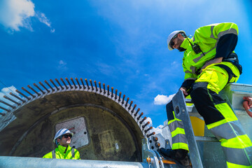 Two engineers in safety gear inspecting a wind turbine blade section on a construction site. They examine the metal framework with precision. Renewable energy project under a clear blue sky.
