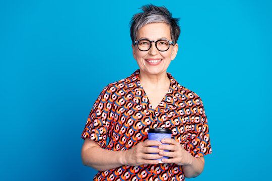 Smiling Mature Woman in Colorful Patterned Shirt Holds a Coffee Cup Against a Bright Blue Background