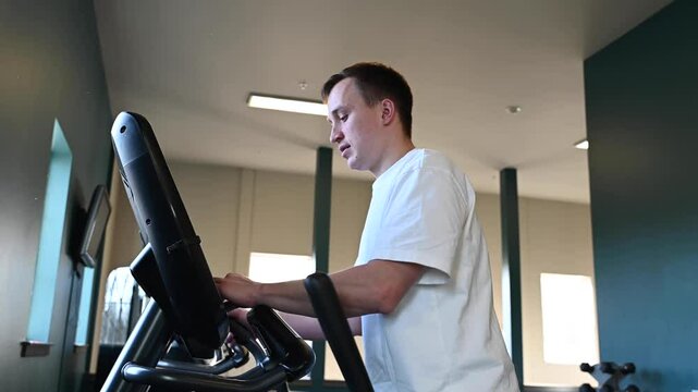 The beginning of a workout in the gym, a young athlete starts training on an elliptical machine.