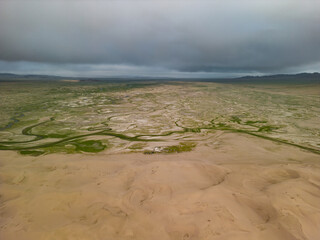 A view from a quadcopter of a desert with dunes and plants during the beginning of the rain. View of the desert from a quadcopter. The beginning of a thunderstorm in the desert.