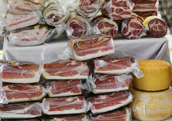 pecorino cheese and many vacuum-sealed and plastic-wrapped cured meats for sale at the market stall