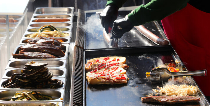 chef wearing gloves prepares sandwiches on the hot griddle with pork sausages and mixed vegetables cooking