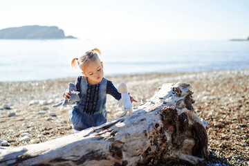 Little girl plays with soft toys moving them on a snag by the sea