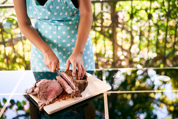Cook cuts the roast beef with blood on a wooden board on the table on the balcony. Cropped