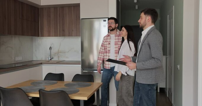 Real estate agent man shows modern house to a young couple. Young couple client rent investment.