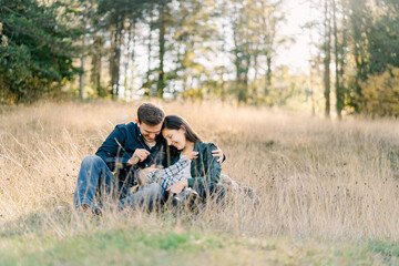 Dad tickles a little girl lying on his and mom knees with a blade of grass