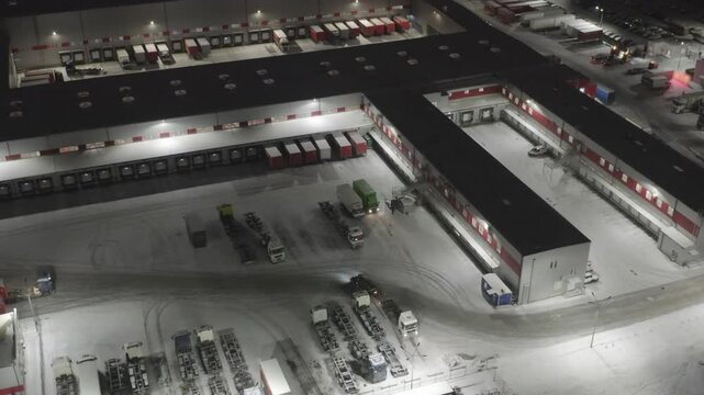 Aerial View of Logistics Hub at Night with Snowy Truck Yard. Large Distribution Center with Loading Docks, Semi-Trucks and Warehouse Operations in Winter