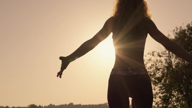 The beautiful silhouette of a woman engaging in a yoga practice at sunset creates a calming atmosphere that promotes the harmony of body and mind while embracing the tranquility of nature