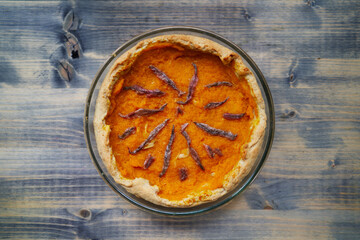 Pumpkin pie with anchovies in a glass dish stands on a wooden table. Top view