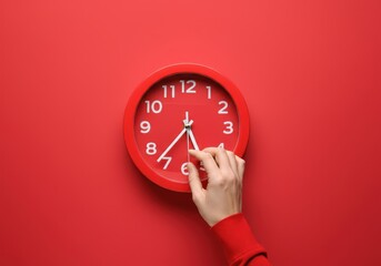 Female professional aligning red clock hands against vivid backdrop, representing workplace time optimization and organizational efficiency
