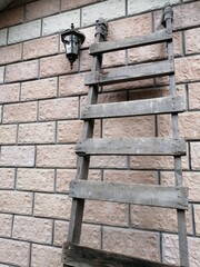 A makeshift old wooden staircase is leaning against the wall of a building made of concrete blocks. There is a beautiful lantern on the facade.