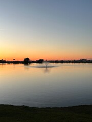 the sunrise is lighting the horizon in shades of pink and orange over a lake with a fountain flowing in the center