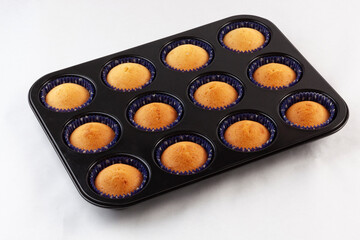 Homemade muffins in a mold and freshly baked on a baking sheet on a white background. Close-up,...
