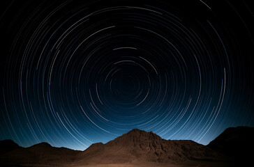 Fototapeta premium Star Trails over Mountains: A mesmerizing long exposure captures the Earth's rotation, painting circular star trails above a serene mountain landscape.