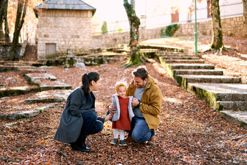 Dad hugs a little girl standing next to him with mom squatting in the forest