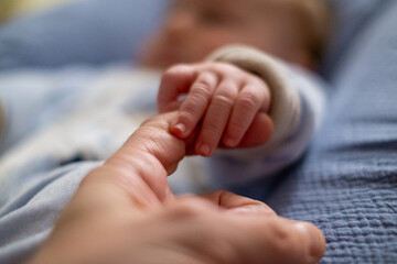 Newborn holding parent's finger with hand