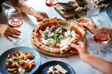 Fototapete Friends enjoy a dinner party with pizza and rose wine in a bar or a restaurant. © FornStudio