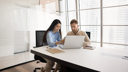 Internship and mentoring. Young Asian female expert mentor help European male intern colleague at...