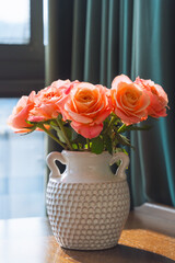 A beautiful bouquet of pink rose flowers in the vase on the wooden table under the sunlight.