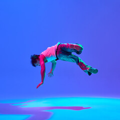Young man, breakdancer mid-performance, bending gravity with skillful moves against gradient blue...