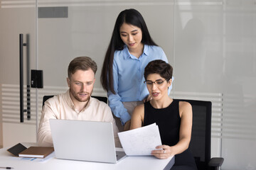 Collaborative work. Focused group three diverse multiethnic employees business team with young woman leader develop document text analyze financial report conduct research using notebook at workplace