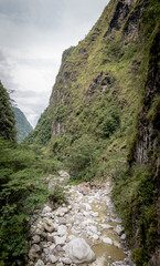 Serene rocky river flowing through a lush green valley, surrounded by towering cliffs and misty skies