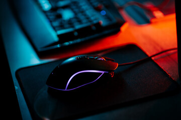 Colorful gaming mouse with neon lighting next to a keyboard on a workstation at night