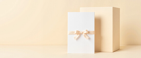 Elegant blank card with ribbon and box on soft ivory background, branding