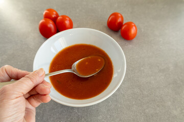 A close-up of a homemade tomato soup served in a white bowl, with a spoon scooping a portion. 