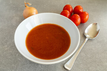 Homemade tomato soup in a white bowl with fresh tomatoes and onion.