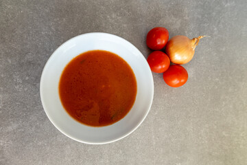 Homemade tomato soup in a white bowl with fresh tomatoes and onion.