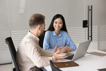 Obraz premium Professional consultation. Confident young businessman sitting at office table consulting young Asian female client colleague explain project agreement details using notebook pc express expert opinion