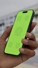 GREEN SCREEN CHROMA KEY Person holding a smartphone with a green screen on a busy urban street featuring colorful buildings and traffic in the background