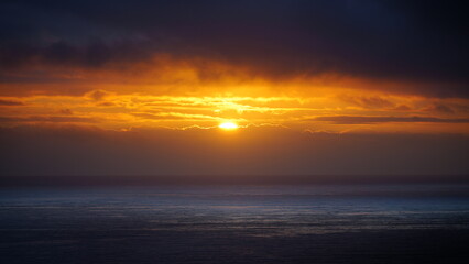 Obraz premium vivid orange sunset over the Atlantic Ocean, with the sky glowing in rich hues as the sun dips below the horizon