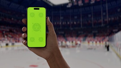 GREEN SCREEN CHROMA KEY A hand holding a phone with a green screen at a hockey game in an indoor stadium, ideal for showcasing live sports or betting apps