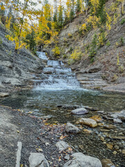 Cascading waterfall in rocky terrain surrounded by autumn trees