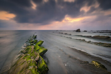 Sunset on Barrika beach with the water running between the rocks on the shore of the Cantabrian Sea