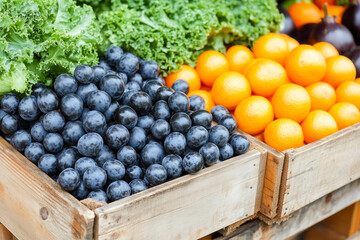 Fresh kale, juicy blueberries, and vibrant oranges in wooden crates at market