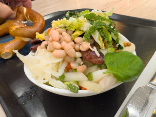 Fresh mixed salad bowl with beans, vegetables, and pretzel on tray