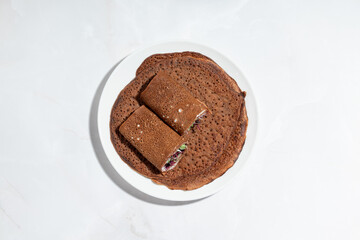 A plate of traditional brown buckwheat crepes with a stuffed rolled version on top, filled with fresh greens and creamy spread.