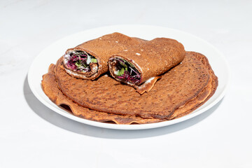 A detailed close-up of stuffed buckwheat crepes, revealing a fresh salad mix and creamy spread inside.