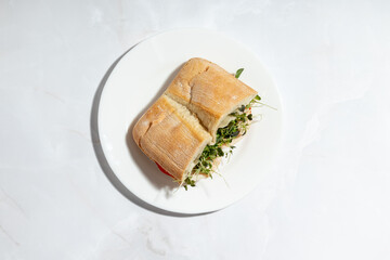 A fresh sandwich with ciabatta bread, turkey, tomato slices, mayonnaise, and microgreens, served on a white plate.