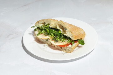 A turkey and microgreens sandwich on a crusty ciabatta roll, presented on a clean white plate.
