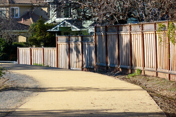 A wooden fence with lattice tops lines a curved dirt pathway, bordered by sparse vegetation, in a...