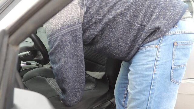 A male craftsman with an injured arm puts a seat cover on a car. The left arm is deformed. The concept of equal opportunities for the disabled.