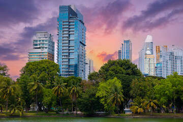 Lumpini Park Bangkok skyline at sunset: urban high-rise buildings and lush park landscape