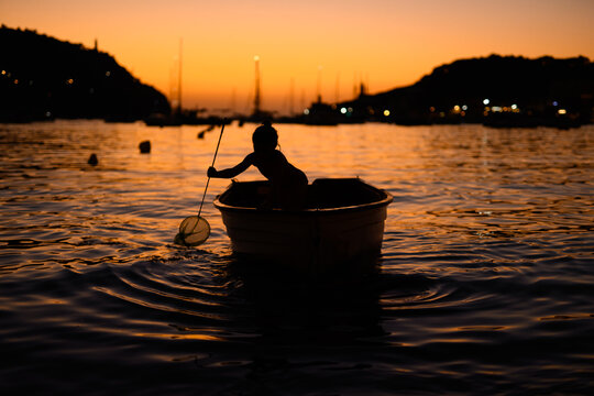 Child in a small boat enjoying sunset on calm waters in Soller